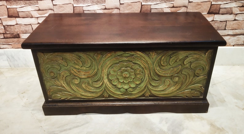 May include: A wooden storage chest with a dark brown finish and intricate green floral carvings. The chest has a hinged lid and a decorative base.