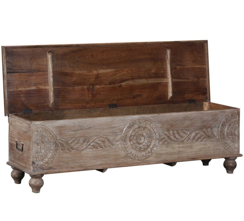 May include: A carved wooden storage bench with a light brown finish. The bench has a hinged lid and four turned legs. The lid is open, revealing the interior of the bench.