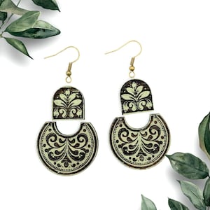 May include: A pair of wooden earrings with a green and brown floral design. The earrings are made of two pieces, a smaller arch-shaped piece and a larger crescent-shaped piece.