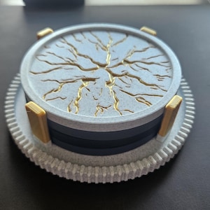 May include: A round, multi-layered coaster set. The top layer is light blue with a gold lightning bolt design. The coaster has gold corner accents and a white, gear-shaped base. The coaster set is designed to protect surfaces from drink rings.