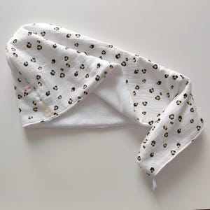 Könnte beinhalten: Weißes Haartuch mit Leopardenmuster in Schwarz und Beige. Das Handtuch hat einen Knopfverschluss und eine Schlaufe zum Aufhängen. Das Handtuch ist aus weichem, saugfähigem Material.