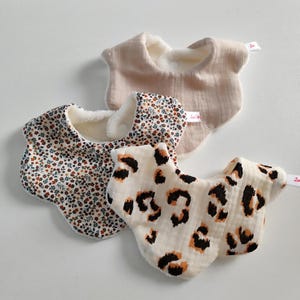 Op de afbeelding: Drie baby slabbetjes in verschillende patronen. Eén is effen beige, een andere heeft een bloemenpatroon met rode en bruine bloemen, en de derde heeft een crèmekleurige achtergrond met bruine luipaardvlekken. Elk slabbetje heeft een zachte, witte binnenkant.