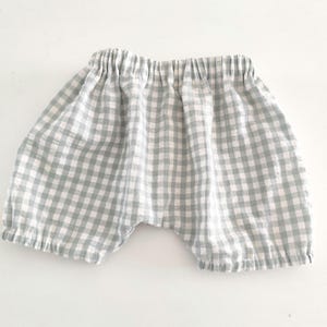 Peut inclure: Shorts à carreaux vichy verts et blancs. Ils ont une taille élastique et une coupe ample et confortable. Le tissu semble léger, adapté aux températures chaudes. Ces shorts sont conçus pour un usage décontracté.