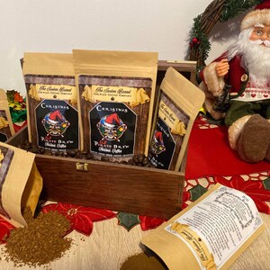May include: A wooden box filled with six bags of Christmas themed coffee. The bags are brown with a red and white design and the text "Christmas Elf Pirate Brew" printed on them. The box is sitting on a red and white tablecloth.