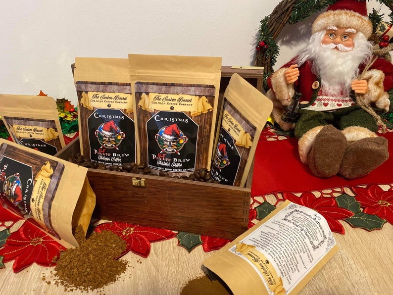 May include: A wooden box filled with six bags of Christmas themed coffee. The bags are brown with a red and white design and the text "Christmas Elf Pirate Brew" printed on them. The box is sitting on a red and white tablecloth.