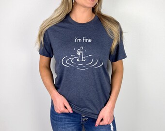 May include: A navy blue t-shirt with a white graphic of a hand giving a thumbs up, with only the thumb sticking out of the water. The text "i'm fine" is above the graphic.