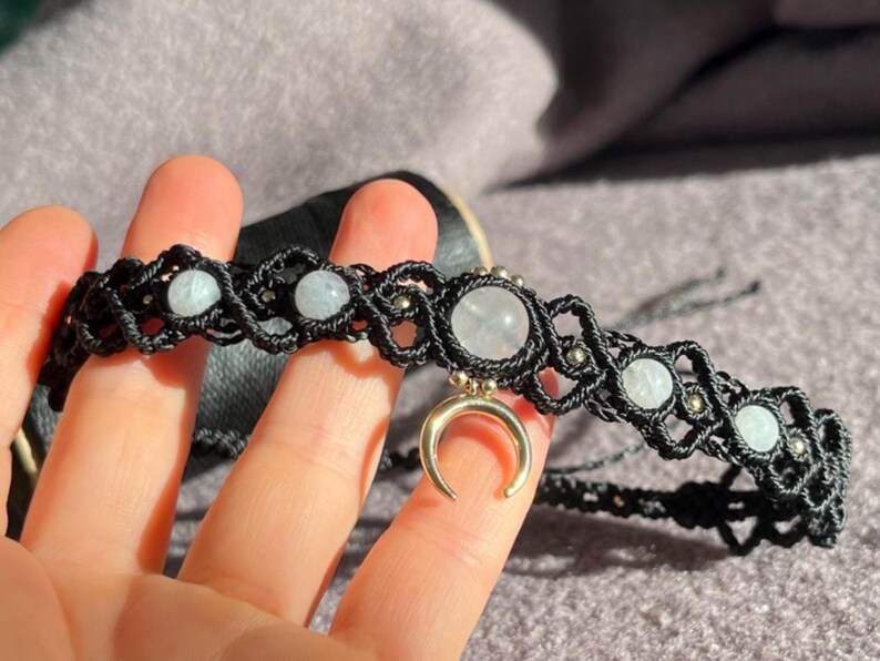 Puede incluir: Collar gargantilla de macram&eacute; negro con piedras preciosas azul claro y blancas y un dije de media luna dorada. El collar presenta un dise&ntilde;o tejido con peque&ntilde;as cuentas met&aacute;licas, creando una est&eacute;tica bohemia.