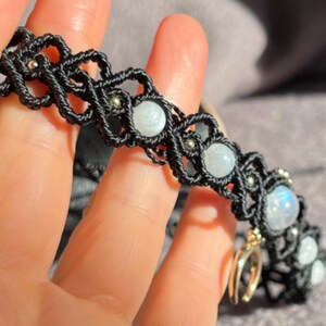 Puede incluir: Pulsera de macram&eacute; negro con cuentas de piedra lunar y detalles plateados. El intrincado dise&ntilde;o tejido resalta la belleza natural de la piedra lunar, creando un accesorio &uacute;nico. Una adici&oacute;n elegante a cualquier colecci&oacute;n de joyas.