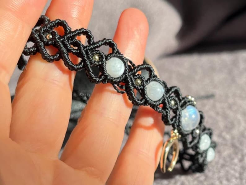 Puede incluir: Pulsera de macram&eacute; negro con cuentas de piedra lunar y detalles plateados. El intrincado dise&ntilde;o tejido resalta la belleza natural de la piedra lunar, creando un accesorio &uacute;nico. Una adici&oacute;n elegante a cualquier colecci&oacute;n de joyas.