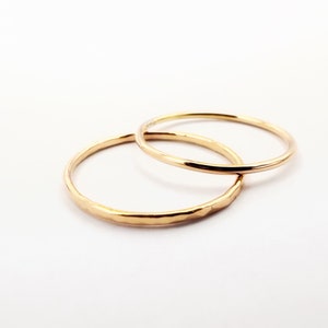 Puede incluir: Dos anillos de oro, uno con un acabado liso y el otro con una textura martillada, están apilados uno encima del otro.