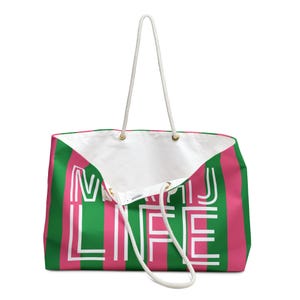 May include: A large tote bag with a white rope handle. The bag features vertical stripes in green and pink, with the words "MAJ LIFE" in white block letters. The interior is white.