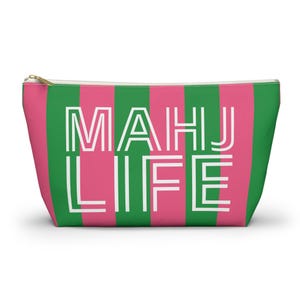 May include: A rectangular cosmetic bag with a pink and green striped pattern. The bag features the white text "MAHJ LIFE" in a bold, sans-serif font. The zipper is gold-colored.