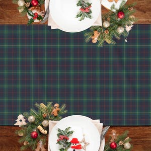 May include: A Christmas table setting with a green, navy, and red plaid table runner. White plates are set with festive decorations, including gingerbread men, holly, and ornaments. The wooden table adds a warm, rustic touch.