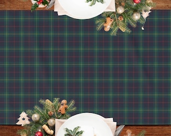 May include: A festive Christmas table setting featuring a green, navy, and red tartan table runner. White plates are adorned with decorations like gingerbread men, holly, and baubles. The wooden table provides a warm, rustic feel.