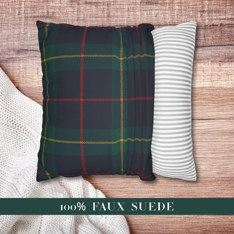 May include: A square throw pillow featuring a dark navy blue, forest green, and red plaid pattern with thin yellow lines, paired with a side panel of white and gray horizontal stripes. The text 100% FAUX SUEDE is printed at the bottom.