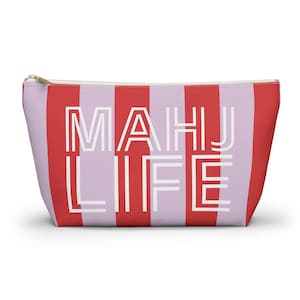 May include: A zippered pouch with a red and lavender striped pattern. The words "MAHJ LIFE" are printed in white block letters across the front. The pouch has a gold-colored zipper.
