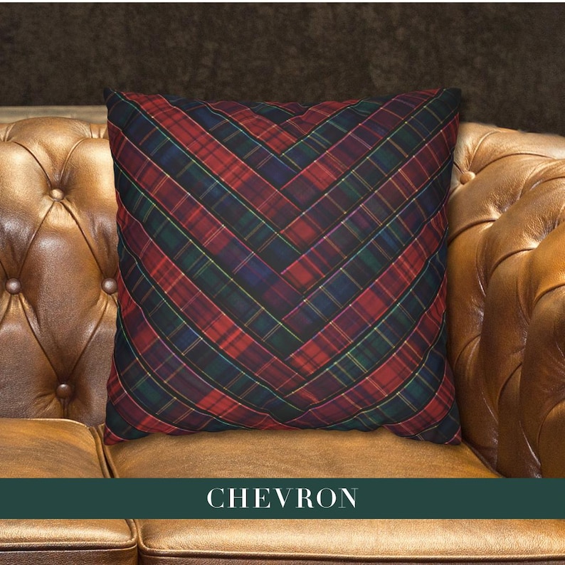 May include: A square throw pillow featuring a dark red, navy blue, and forest green plaid pattern arranged in a chevron design. The fabric displays a woven texture with thin yellow accent lines running through the tartan grid, creating a geometric effect.