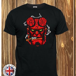 Op de afbeelding: Zwart T-shirt met een rode illustratie van Hellboys gezicht, met het woord "Hellboy" in rode letters boven zijn hoofd. De illustratie toont Hellboy met een sigaar in zijn mond en een serieuze uitdrukking. Het T-shirt heeft een klein label onderaan met de tekst "Made in the UK, Manufactured in Britain."