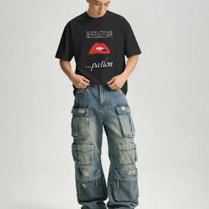 May include: A black short-sleeved t-shirt featuring a graphic of red lips and the text "...pation" below, paired with loose-fitting blue denim cargo trousers that have multiple large pockets and distressed details on the fabric surface.