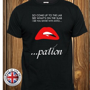 May include: A black short-sleeved t-shirt featuring a graphic of bright red lips with white teeth. The text reads: SO COME UP TO THE LAB SEE WHAT'S ON THE SLAB I SEE YOU SHIVER WITH ANTICI... ...pation. A circular badge with the UK flag is in the corner.