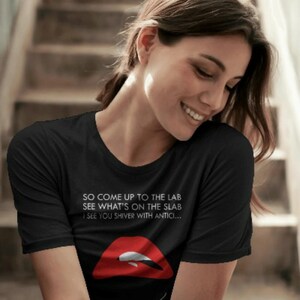 May include: A black short-sleeved t-shirt featuring white text that reads SO COME UP TO THE LAB SEE WHAT'S ON THE SLAB I SEE YOU SHIVER WITH ANTICI... above a graphic of red lips with white teeth. The shirt has a crew neckline and a standard fit.