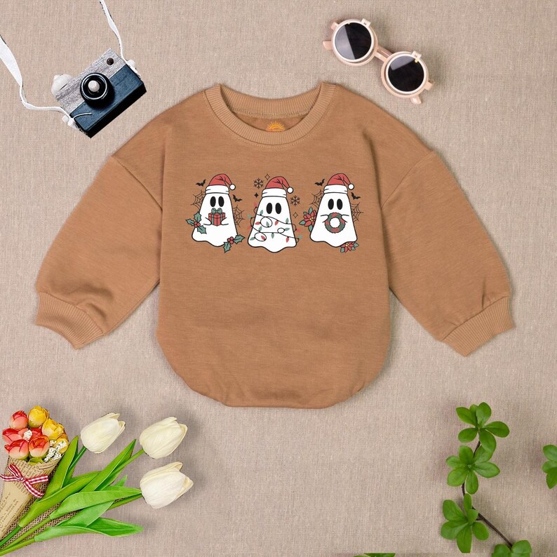 Puede incluir: Una sudadera marr&oacute;n de manga larga con un dise&ntilde;o de fantasma navide&ntilde;o. Los fantasmas llevan gorros de Pap&aacute; Noel y tienen decoraciones festivas como regalos, luces y coronas.