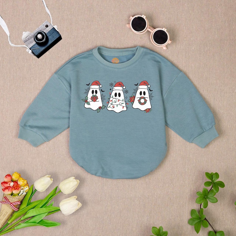 Puede incluir: Una sudadera azul claro con un dise&ntilde;o de fantasma navide&ntilde;o. Los fantasmas llevan gorros de Pap&aacute; Noel y sostienen decoraciones navide&ntilde;as.