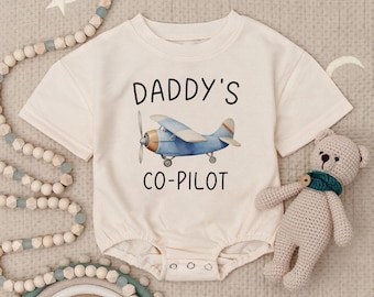 May include: A white baby onesie with short sleeves features a blue airplane graphic and the text "Daddy's Co-Pilot".