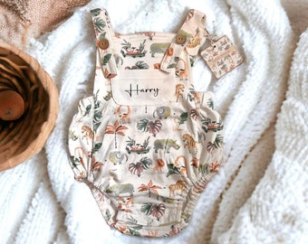 May include: A cream-colored baby onesie with a jungle animal print. The onesie has adjustable straps and a pocket on the front. The name "Harry" is embroidered on the pocket.