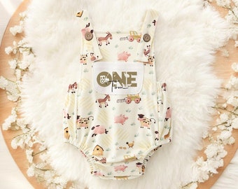 May include: A white baby onesie with a farm animal print. The onesie has a brown patch with the word "ONE" and a small tractor graphic.
