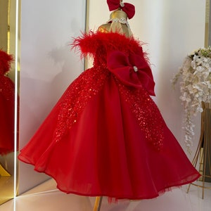 Puede incluir: Un vestido de tul rojo con un gran lazo rojo y ribete de plumas. El vestido est&aacute; decorado con lentejuelas y tiene una falda completa.