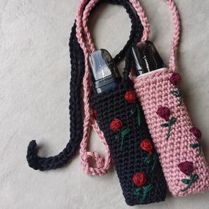 May include: Two crochet vape holders, one black and one pink, each with a matching strap. The black holder has red rose embroidery, while the pink one has burgundy roses. Both are designed to hold a vape device.