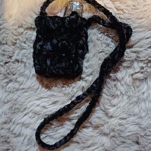 Może przedstawiać: Mała, czarna, pluszowa torba z długim paskiem. Torba wykonana jest z miękkiego, puszystego materiału, prawdopodobnie do przenoszenia małego przedmiotu. Pasek r&oacute;wnież wykonany jest z tego samego materiału.