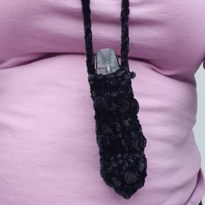 Może przedstawiać: Czarny, pluszowy, szydełkowy uchwyt na vape z pasującym sznurkiem, noszony na szyi. Uchwyt zawiera przezroczyste urządzenie vape. Tło to jasnor&oacute;żowa koszula.