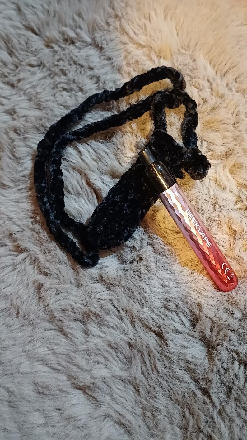 Może przedstawiać: R&oacute;żowy i srebrny długopis Geekvape vape z czarnym aksamitnym etui i smyczą. Pi&oacute;ro ma geometryczny wz&oacute;r i napis "GEEKVAPE". Smycz i etui są wykonane z miękkiego, pluszowego materiału.