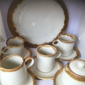 May include: A set of white ceramic teacups and saucers with brown trim. The set includes a large platter with a brown rim.