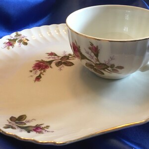 May include: A white porcelain teacup and saucer set with a rose floral design. The saucer is shaped like a shell and has a gold trim.