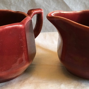 May include: A set of two red ceramic creamer and sugar bowls with octagonal sides and a glossy finish.