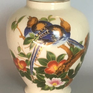 May include: A white ceramic vase with a gold rim and a floral design featuring blue and gold birds, green leaves, and red and pink flowers.