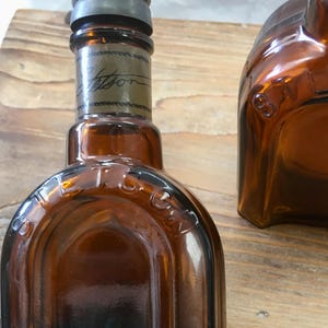 May include: Amber-colored glass bottles with metal caps. One bottle has the word "Stetson" printed on it. The bottles are on a wooden surface. The bottles have a vintage appearance.