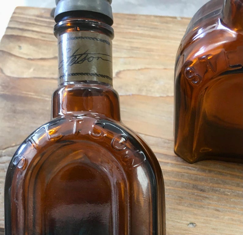 May include: Amber-colored glass bottles with metal caps. One bottle has the word "Stetson" printed on it. The bottles are on a wooden surface. The bottles have a vintage appearance.
