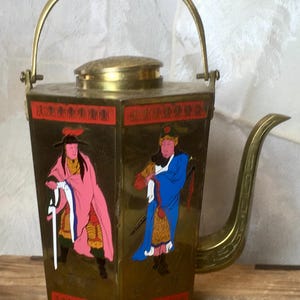 May include: A hexagonal brass teapot featuring a swing handle, a curved spout, and a lid. The body is decorated with two painted figures in traditional attire, one in a pink robe and one in a blue robe, set against a metallic brass background.