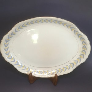 May include: A white oval serving platter with a blue and yellow floral border. The platter is on a wooden stand.