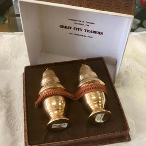 May include: Two gold-colored, decorative items with a bulbous base and a conical top, wrapped with a red-brown ribbon, presented in a box. The box is labeled "Great City Traders, San Francisco, CA, 94103."