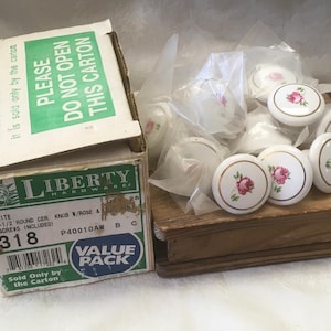 May include: A cardboard box labeled Liberty Hardware containing 25 round ceramic knobs with a rose pattern and gold ring detail. The box features text including "PLEASE DO NOT OPEN THIS CARTON" and "1-1/2 INCH ROUND CER. KNOB W/ROSE & GOLD RING".