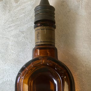 May include: Close-up of a vintage brown glass cologne bottle with a metal cap. The bottle has a label with the word "COLOGNE" visible. The bottle's shape is rounded at the bottom and tapers towards the top.