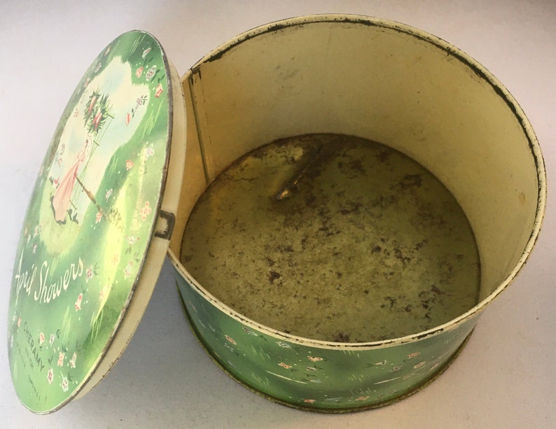 May include: A vintage green and white tin box with a floral design and the text "April Showers" on the lid. The lid is open and the inside of the box is visible.