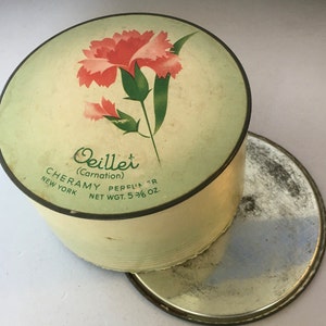 May include: A vintage round powder compact with a green and white lid. The lid features a pink carnation flower with green leaves and the text "Oeillet (Carnation) CHERAMY PERFUMER NEW YORK NET WGT. 5 3/8 OZ."