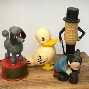 May include: A set of four vintage plastic figurines: a gray poodle, a white duck, a peanut-shaped figure wearing a top hat, and a black and white Mickey Mouse figure.