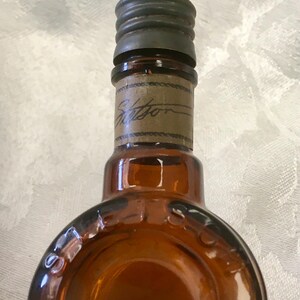 May include: An antique brown glass bottle with a dark metal cap and a paper label. The label has the word "Stetson" written on it. The bottle has a rounded shape and is likely from the early 20th century.